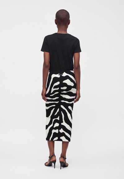 Personne portant un haut noir à manches courtes et une jupe midi taille haute à rayures zébrées noires et blanches, avec des sandales noires à talons hauts.