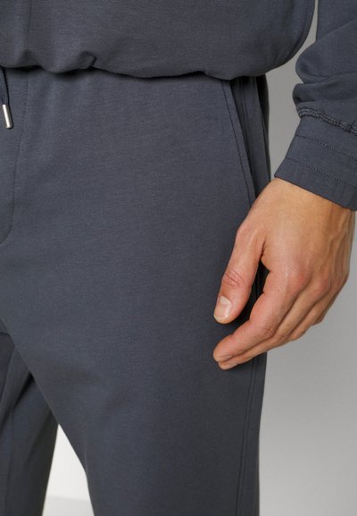 Joggers de algodão cinza misto, com cintura elástica ajustável, textura suave e punhos elásticos. Mão apoiada na área da coxa.