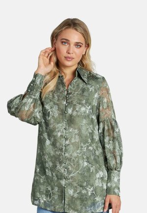 Blusa verde con estampado floral, con cuello tipo solapa, botones en la parte delantera y mangas abullonadas, hecha de una tela transparente.
