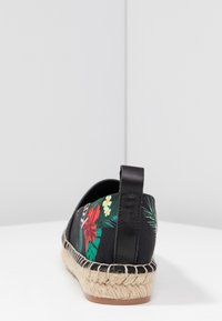 Espadrille negra con un patrón floral que presenta flores rojas y amarillas, suela de yute de cuerda y acentos de cuero en la parte trasera.