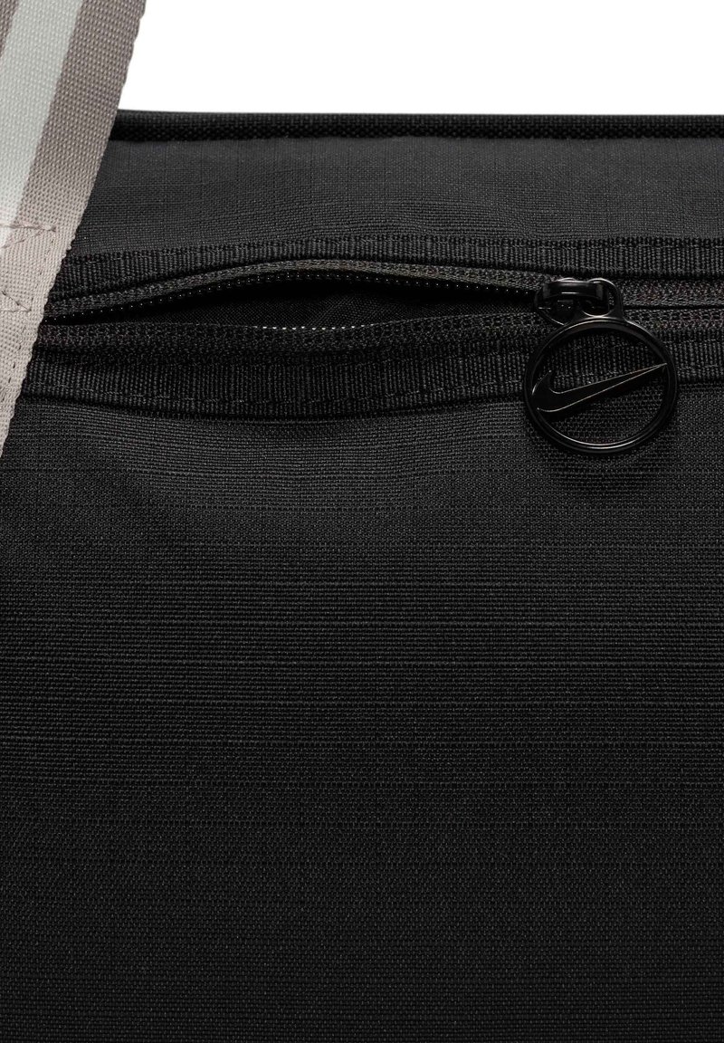 Bolsa de tela negra con una superficie texturizada, que presenta un cierre de cremallera y un tirador de cremallera circular negro con un detalle del logotipo.