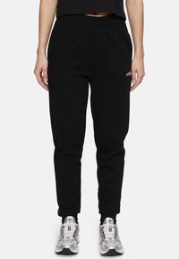 Zwarte sweatpants met een elastische tailleband, taps toelopende pijpen en een klein rood en wit FILA-logo op de linkerdij, gecombineerd met stevige sneakers.