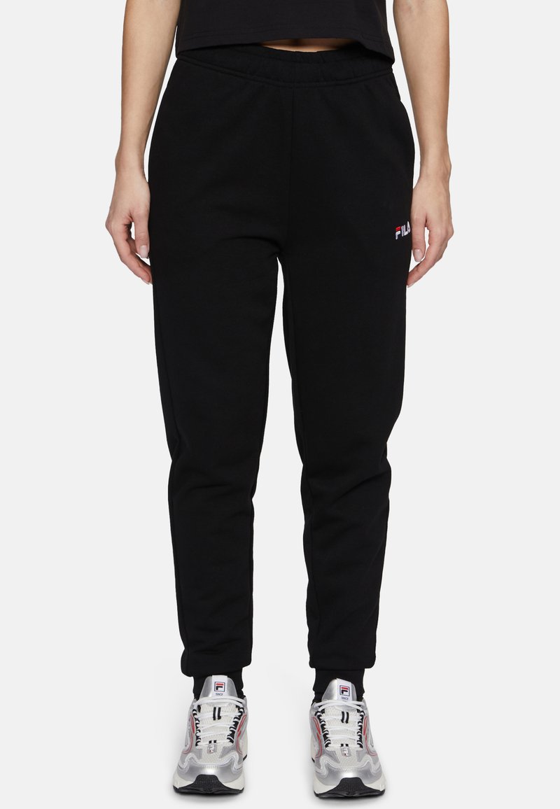Zwarte sweatpants met een elastische tailleband, taps toelopende pijpen en een klein rood en wit FILA-logo op de linkerdij, gecombineerd met stevige sneakers.