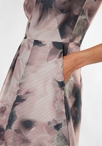 Hihaton mekko teksturoidusta kankaasta, jossa on sekoitus hillittyjä vaaleanpunaisia, kermaisenvärisiä ja tummia kukkakuoseja, sekä näkyvä sivutasku.