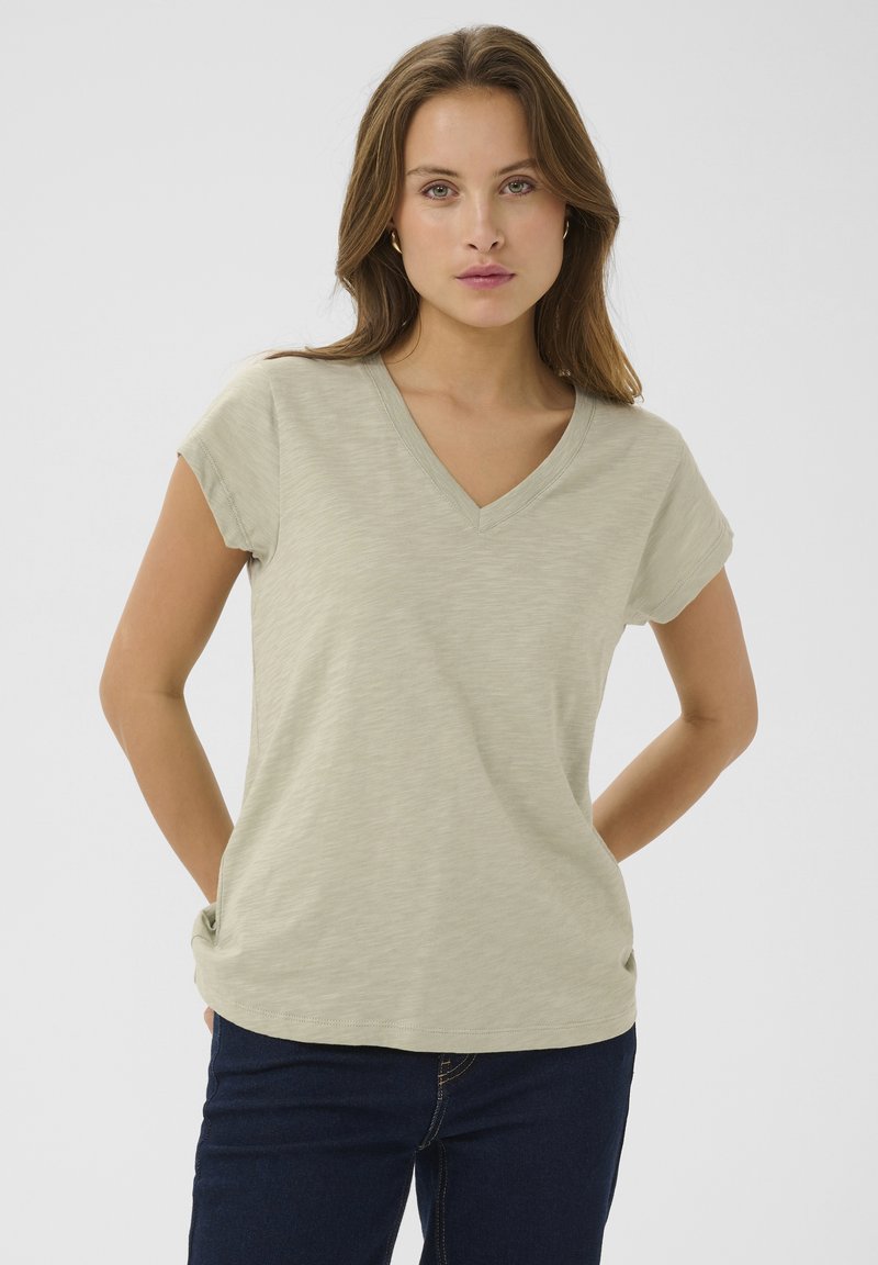 Ljus olivgrön T-shirt med V-ringning i mjukt tyg, med rullade korta ärmar och en avslappnad passform, tillsammans med mörka jeans.