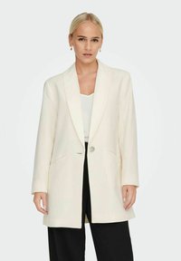 Blazer ivoire avec un col cranté, fermeture à un bouton, deux poches avant et manches longues ; texture lisse, coupe légèrement oversize.
