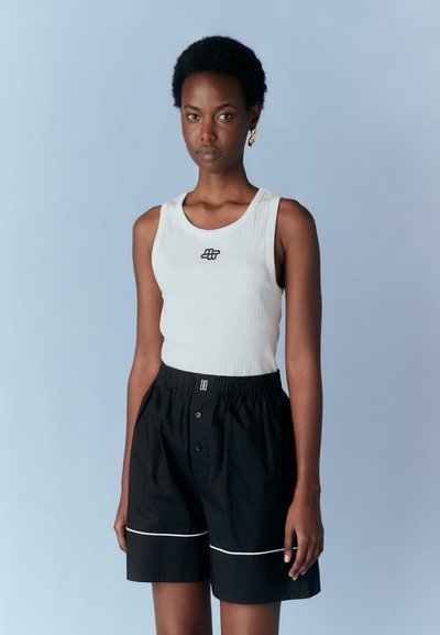Débardeur côtelé blanc avec un logo noir, associé à un short noir avec une taille élastique, des boutons et un passepoil blanc le long de l'ourlet.