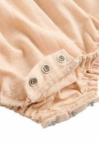 Tissu de couleur pêche avec un motif en grille, présentant un bord froncé et trois boutons-pression en argent en bas.