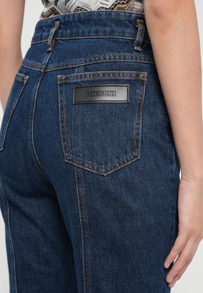 Jeans en denim bleu foncé à taille haute, dotés d'un logo en cuir noir sur la poche arrière et de détails de surpiqûres contrastants.