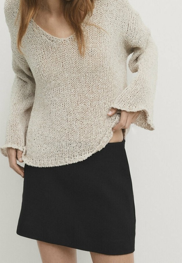Beige knit sweater with a loose fit and bell sleeves, paired with a black mini skirt. The sweater features a V-neck and a textured pattern.