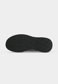 Semelle d'une chaussure noire avec une surface en caoutchouc texturée antidérapante, présentée sur fond blanc.