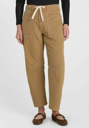 Pantaloni marroni a gamba dritta con grandi tasche frontali e vita con coulisse bianca, indossati con scarpe Mary Jane marrone scuro.