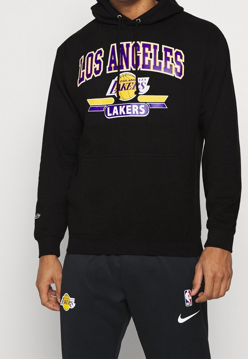 Felpa nera con cappuccio che presenta la scritta "LOS ANGELES LAKERS" in testo giallo e viola. Il tessuto è morbido, con una tasca frontale e un cappuccio regolabile con cordino.