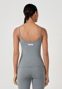 Graues Tanktop aus elastischem Stoff, mit dünnen Trägern und einem tiefen Rückenausschnitt. Ein kleines weißes Etikett ist an der oberen Rückseite sichtbar.