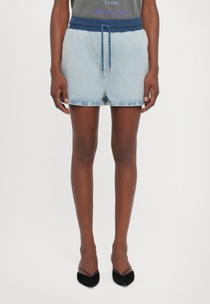Denimshorts med et elastisk marineblå liv, laget med snor. Lys blå farge, frynset kant, sammen med svarte, spisse hæler.