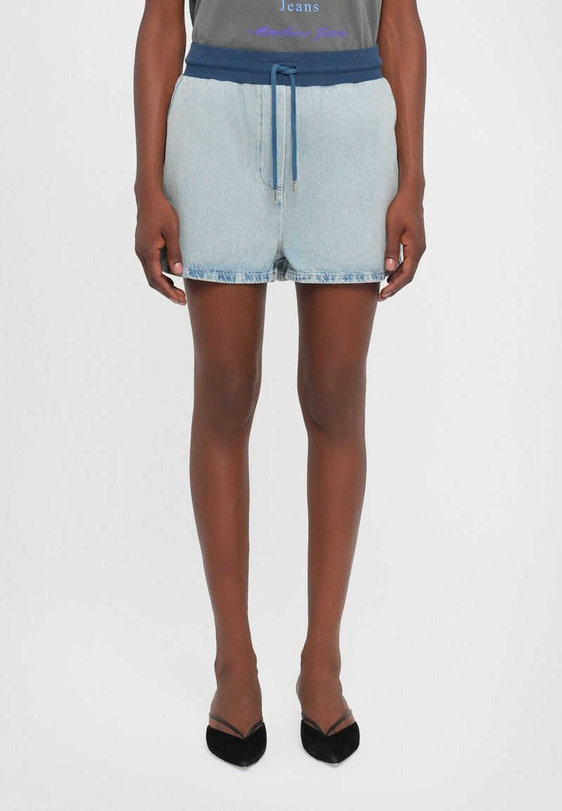 Denimshorts med et elastisk marineblå liv, laget med snor. Lys blå farge, frynset kant, sammen med svarte, spisse hæler.