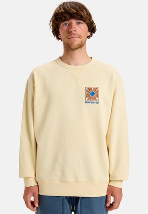 Cream-colored sweatshirt with a round neckline, ribbed cuffs, and a square embroidered patch featuring a sun design and logo on the chest.