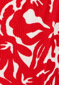 Rode stof met een gedurfde witte abstracte bloemenpatroon en een textuur met een gekreukt oppervlak. Het ontwerp benadrukt contrast en visuele interesse.