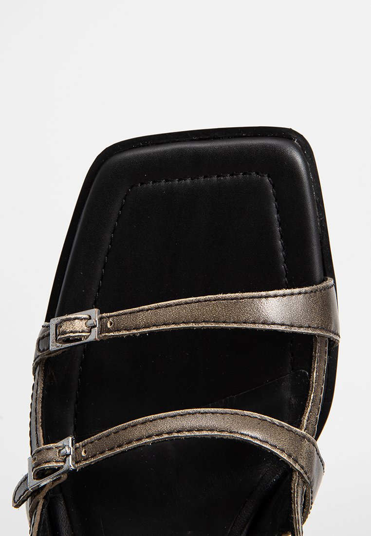 Sandale noire à bout carré avec deux brides grises métalliques, chacune dotée d'un petit boucle en argent sur fond blanc.