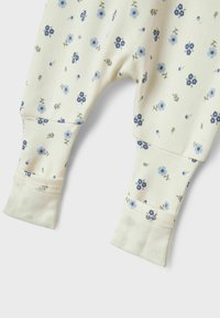 Bebiskläder i bomull i krämfärg med ett blommönster i blått och grönt. Har muddar vid nederkanten och en mjuk textur för komfort.