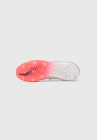 Sole di scarpini da calcio bianca e rosa con tacchetti trasparenti, caratterizzata da una striscia nera e il testo "MESSI". Texture liscia e design dinamico.