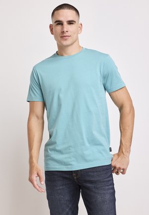 Teal katoenen t-shirt met korte mouwen, ronde hals en een rechte zoom. Gepaard met donkere jeans met subtiele stikseldetails.