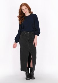 Maglietta a maniche lunghe blu navy con maniche a palloncino, abbinata a una gonna in denim nera con spacco frontale e stivali neri alla caviglia.