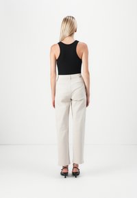 Black fitted tank top paired with beige high-waisted trousers, featuring a smooth texture and straight-leg design, viewed from the back.