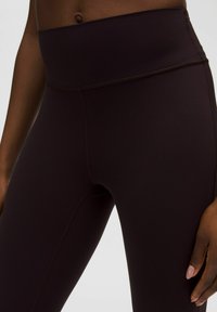 Hoogwaardige, donkerbruine leggings van rekbare stof, met een gladde textuur en platte naden voor comfort en bewegingsgemak.