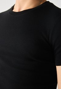 Schwarzes geripptes Kurzarm-T-Shirt. Weicher Stoff und figurnahe Passform mit klassischem Rundhalsausschnitt. Keine sichtbaren Logos oder Muster.