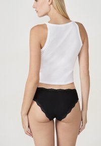 Sous-vêtements noirs bordés de dentelle portée avec un débardeur court blanc. Le tissu semble lisse, avec une coupe ajustée et des bords festonnés.