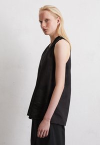 Top noir sans manches en tissu léger avec une coupe décontractée, doté d'un col en V et d'un ourlet légèrement irrégulier pour un look relaxé.