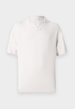 Light pink textured short-sleeve pullover over red and white striped long-sleeve shirt, paired with light beige trousers and black shoes.