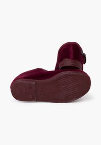 Zapatos de terciopelo burdeos con suela de goma texturizada y un pequeño tacón de madera. El diseño incluye un acento decorativo de hebilla.