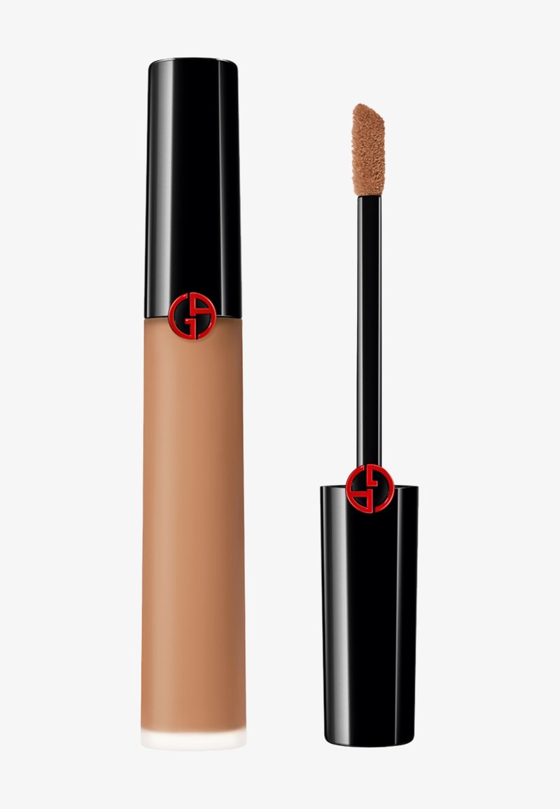 Flytende foundation i en sylinderformet glassflaske. Har et svart hette med en rød logo. Leveres med en applikator med taupe-spiss. Medium brun nyanse.