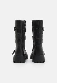 Black leather ankle boots with a chunky sole, featuring vertical zipper, adjustable straps, and textured accents on the shaft.