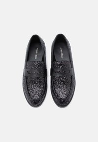 Černé třpytivé loafers s hladkým černým páskem přes přední část. Obsahují polstrovanou stélku a zaoblenou špičku pro pohodlí.