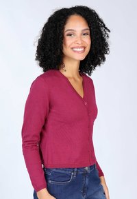 Weinroter Knopf-Cardigan mit V-Ausschnitt, strukturierten Punkten, langen Ärmeln und cropped Passform, kombiniert mit blauen Jeans.