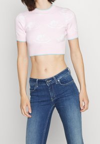 Top de punto corto en rosa claro con mangas cortas, que presenta un patrón de nubes en blanco y un cuello y dobladillo acanalados en azul. Combinado con jeans de mezclilla azul.