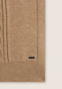 Maglione beige lavorato a maglia con motivo a treccia, orlo a coste e una piccola etichetta con logo. Texture morbida, spessore medio e design classico.