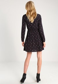 Svart långärmad klänning med blommönster, featuring ett elastiskt midjeband och en utställd kjol. I kombination med svarta ankelboots.