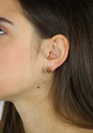 Ohrstecker aus goldfarbenem Metall in Form einer zarten Rose mit übereinanderliegenden Blütenblättern. Glatte Oberfläche und kleine Größe, sichtbar im Ohrläppchen.