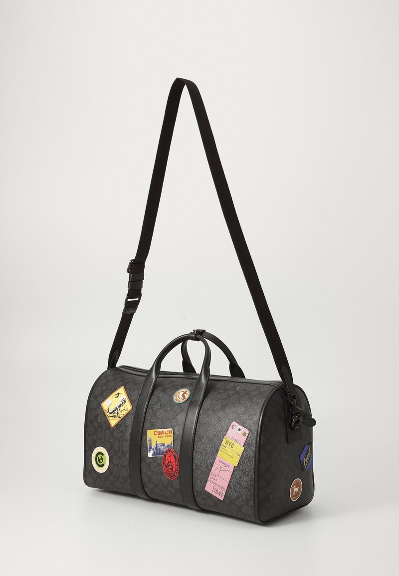 Black leather duffel bag with dual handles and adjustable strap, featuring various colorful travel stickers on its surface.