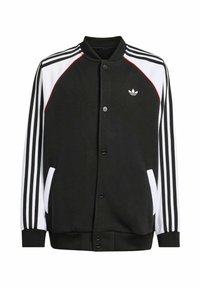 Crna jakna s kopčanjem sprijeda, bijelim i crvenim detaljima te tri vertikalne bijele pruge na svakom rukavu. Ima bočne džepove.