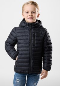 Sort dunjakke med hætte, quiltet design, frontlynlås og brystlomme. Kombineret med slidte blå jeans.