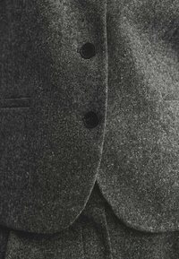 Tummanharmaa bleiseri, joka on valmistettu teksturoidusta kankaasta, jossa on kolme mustaa nappia, lovellinen kaulus ja muotoiltu istuvuus.