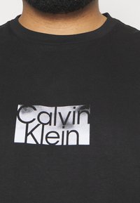 Svart bomull t-shirt med en vit grafisk logotyp med en texturerad design som står "Calvin Klein." Rund halsringning och korta ärmar.