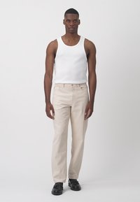 Jeans beige con un diseño de pierna recta, hechos de denim, combinados con una camiseta sin mangas blanca y zapatos negros. La tela parece suave y texturada.