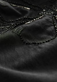 Schwarzer Satin-Stoff mit aufwendiger schwarzer Perlenstickerei und Sticken, die strukturierte Muster mit filigranen Details und glänzenden Akzenten schafft.