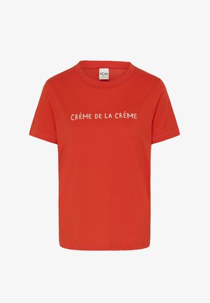 Punane puuvillane T-särk lühikeste varrukatega ja ümarate kaelusega. Esikülge ilmestab valge tekst "CRÉME DE LA CRÉME", mis on keskel.